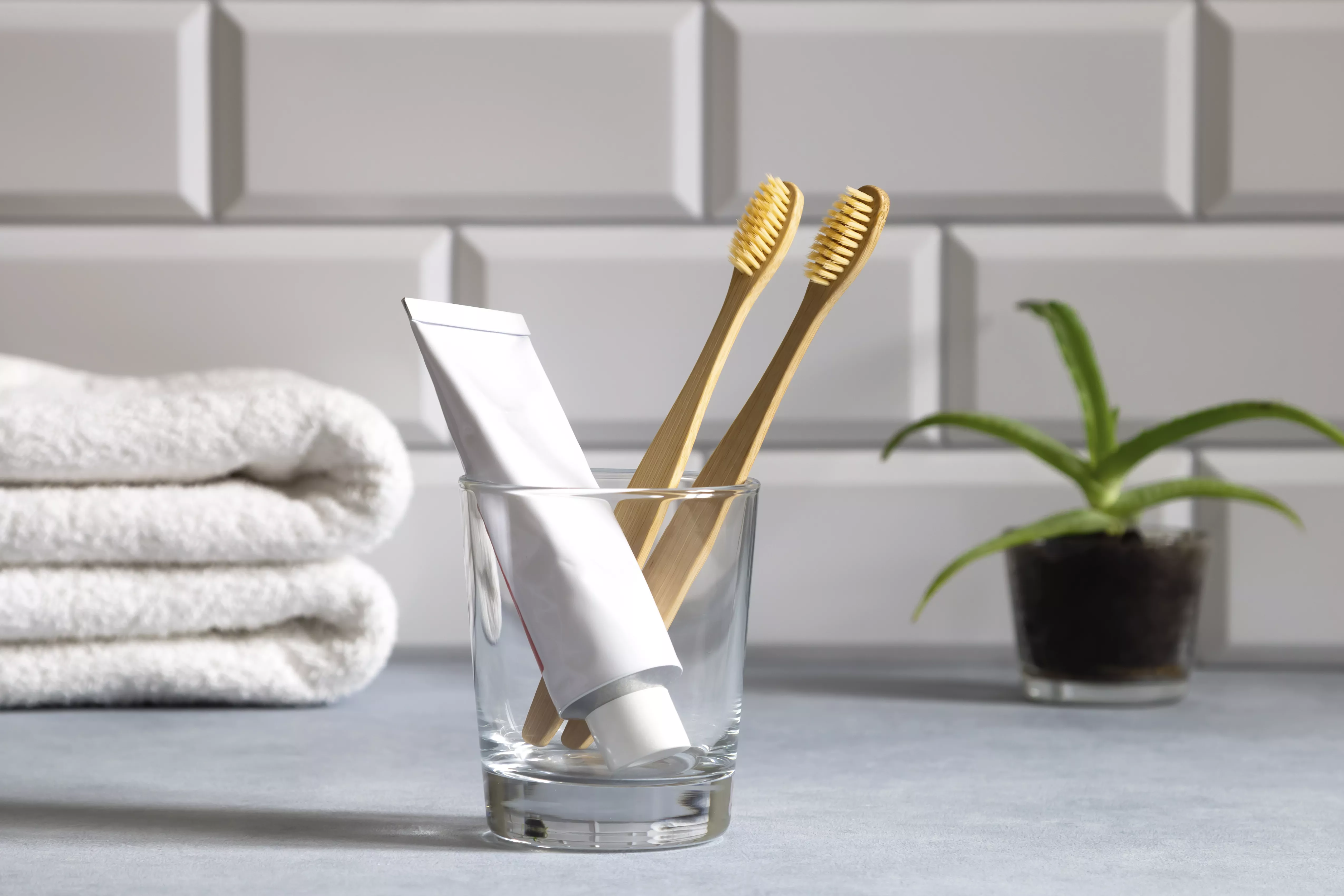 glass with toothpaste and bamboo toothbrushes in tiled bathroom